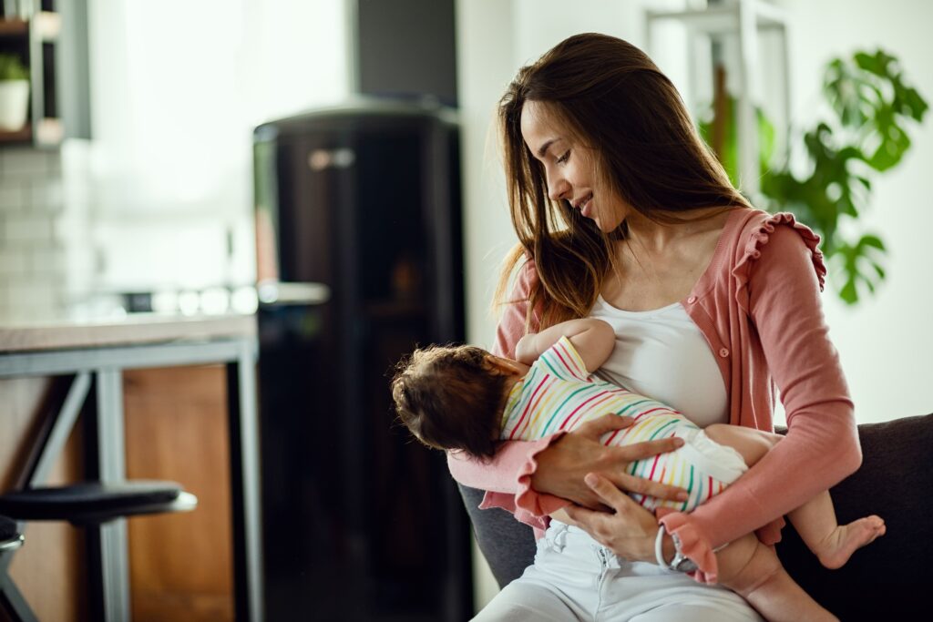 madre sonriente amamantando su hija mientras casa