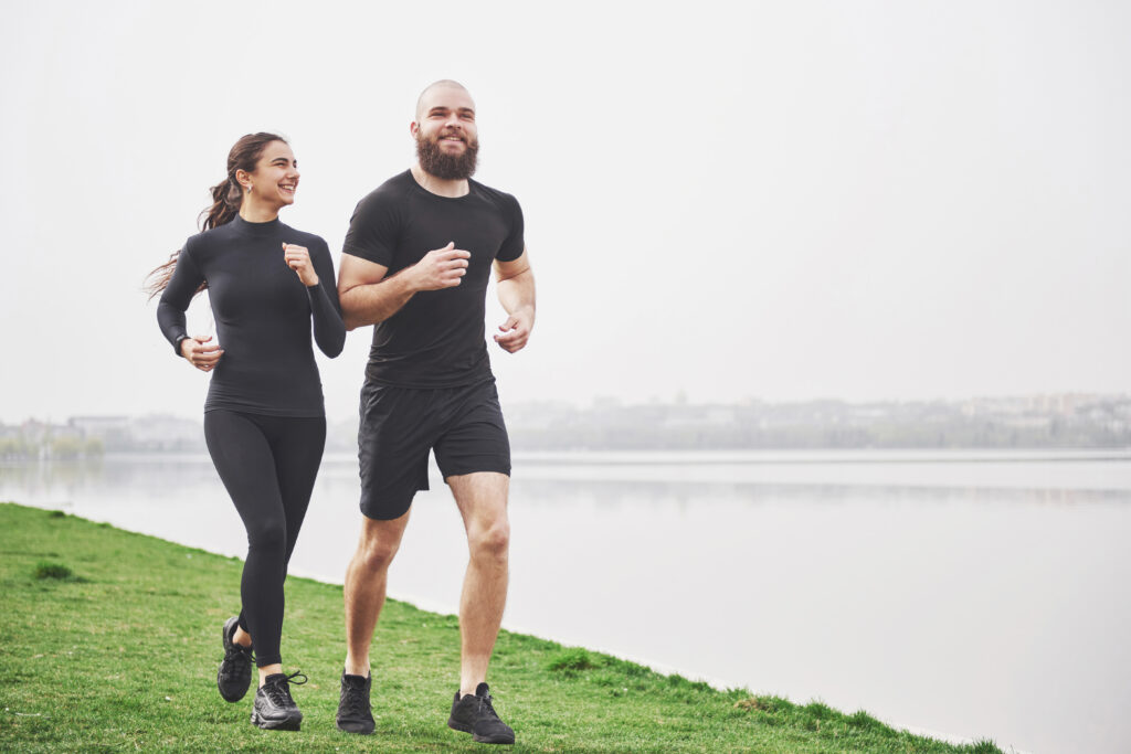 par trotar correr al aire libre parque cerca agua joven barbudo hombre mujer haciendo ejercicio juntos manana